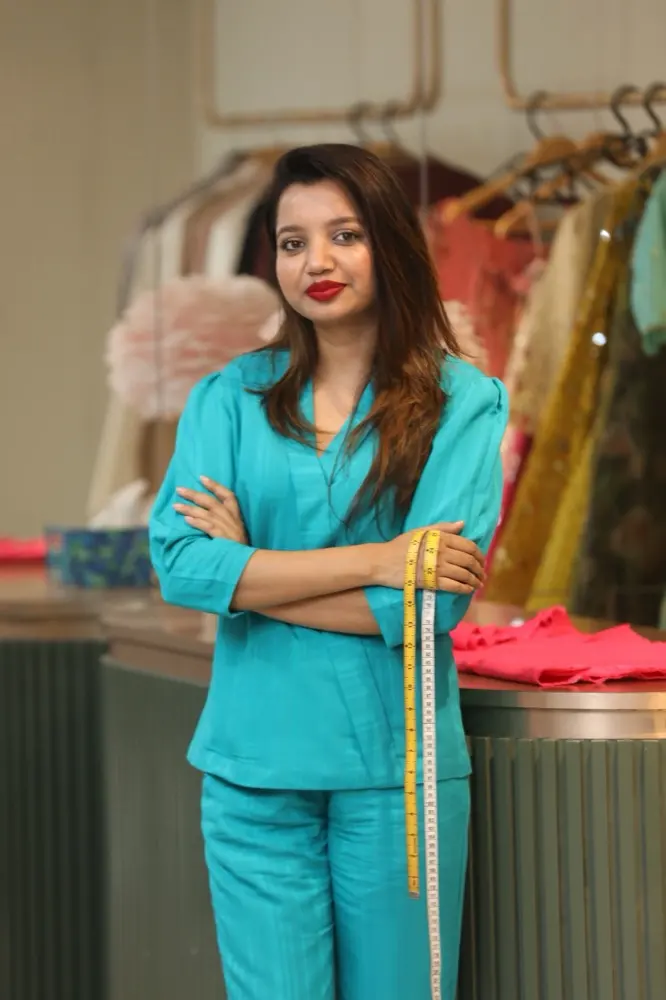 Safia Sathi in her atelier, holding a measuring tape beside her designs